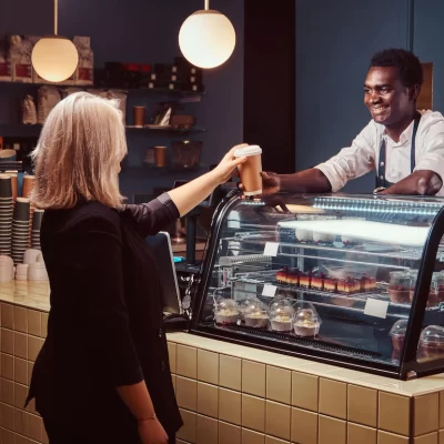 smiling-african-american-barista-uniform-giving-cup-coffee-his-client-trendy-coffee-shop_613910-21068